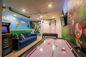 A room with a foosball table, a blue sofa, and a Mario-themed mural.