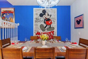 Uma sala de jantar com parede azul, um cartaz do Mickey Mouse e um candelabro.