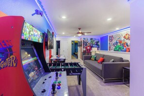 Um quarto com mesa de futebol, sofá com almofadas coloridas e parede com arte de super-heróis.