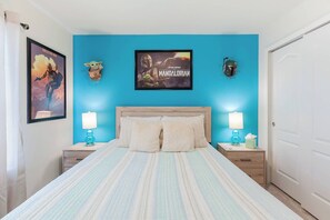 A bedroom with a bed, two nightstands, a wall-mounted lamp, a framed poster, and a door.