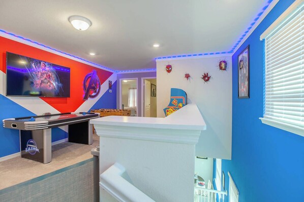 A room with a foosball table, a TV mounted on the wall, and a colorful wall decoration.