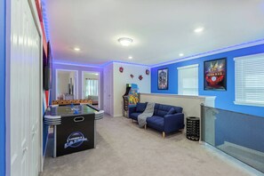 A room with a foosball table, a blue couch, and a wall with framed pictures.