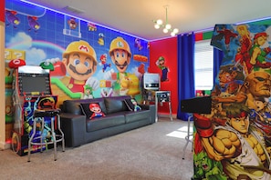 Quarto com sofá, console de jogos e parede decorada com Mario e outros personagens.