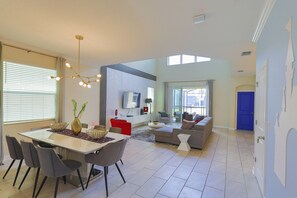 A spacious living area with a dining table, chairs, a sofa, and a television.