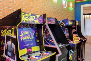 Des bornes d’arcade arborant le logo de « Street Fighter II », un mur de briques et des enseignes au néon en arrière-plan.