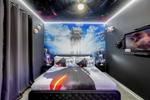 Une chambre avec une fresque murale sur le thème de Star Wars, un lit avec des oreillers assortis et un projecteur au plafond.