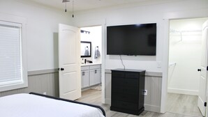 Ein Schlafzimmer mit einem Bett, einer Kommode, einem an der Wand befestigten Fernseher und einer Tür zu einem Badezimmer.