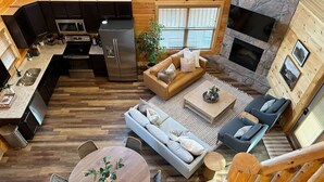 A spacious living area with a kitchen, a round dining table, a sofa, and a fireplace. - Luxury Smoky Mountain Cabin w/ Pool, Arcade, Hot Tub & Scenic Deck (Pigeon Forge)