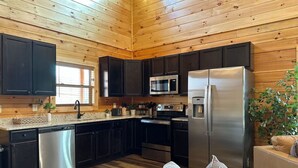 A modern kitchen with dark cabinets, stainless steel appliances, and a wooden ceiling. - Luxury Smoky Mountain Cabin w/ Pool, Arcade, Hot Tub & Scenic Deck (Pigeon Forge)