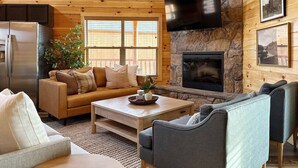 Un salon chaleureux avec une cheminée en pierre, un plafond en bois et un grand téléviseur fixé au-dessus.