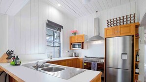 A kitchen with wooden cabinets, a stainless steel refrigerator, a stove, and a sink with a cutting board.