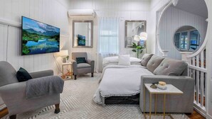 A modern bedroom with a bed, two armchairs, a small table, and a large window with curtains.