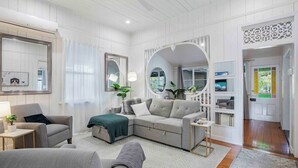 A modern living room with a grey sectional sofa, a small table, and a large mirror. There is a staircase leading to another level, and a door with a decorative glass panel.