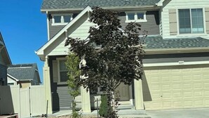 A residential house with a garage, a small tree in the front yard, and a clear blue sky. - Walkout basement and easy access to I-70 and DIA (Denver)