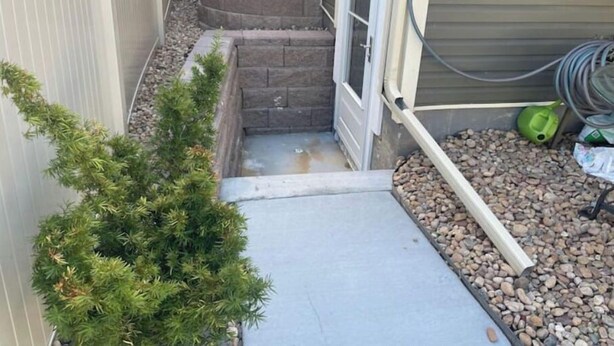 A narrow outdoor pathway leading to a door, flanked by a small tree and a stone planter. - Walkout basement and easy access to I-70 and DIA (Denver)