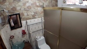 Un baño con pared de piedra, inodoro, lavabo y ducha.