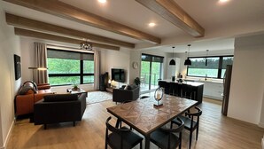 A spacious living area with a wooden dining table, black chairs, a sofa, and a TV. - The JOFORD, Condo, 5 minutes from skiing, Sépaq with extras (bikes, paddles +) (Orford)