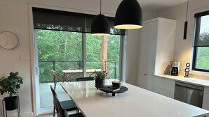 A modern kitchen with a large island, black pendant lights, and a view of greenery outside. - The JOFORD, Condo, 5 minutes from skiing, Sépaq with extras (bikes, paddles +) (Orford)
