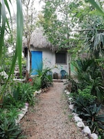 Un sendero en un jardín que lleva a una casa con puerta azul y techo de paja.