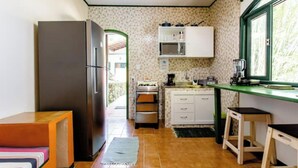 Eine kompakte Küche mit Kühlschrank, Mikrowelle und Herd. Ein Fenster sorgt für natürliches Licht, und ein kleiner Holzschemel steht in der Nähe des Fensters.