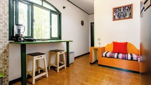 Eine kompakte Küche mit Fenster, zwei Hocker, einer Couch und einem Wandbild.