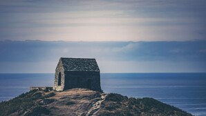 A stone structure with a sloped roof, situated on a hill overlooking a body of water. - Rame View - Double Bedroom with En-suite (Millbrook)