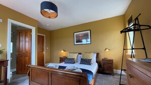 A bedroom with a wooden bed, a ceiling lamp, a nightstand, a dresser, and a window with a view. - Rame View - Double Bedroom with En-suite (Millbrook)