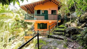 A two-story building with a balcony, surrounded by lush greenery and rocky terrain. - Accès Direct à la Plage - Suite Île (Itacuruçá)