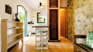A spacious room with a stone wall, a wooden door, and a tiled floor. There is a shelf with books and a small table with a plant. - Accès Direct à la Plage - Suite Île (Itacuruçá)