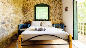A bedroom with a stone wall, a bed with a metal frame, and a window with a green frame. - Accès Direct à la Plage - Suite Île (Itacuruçá)