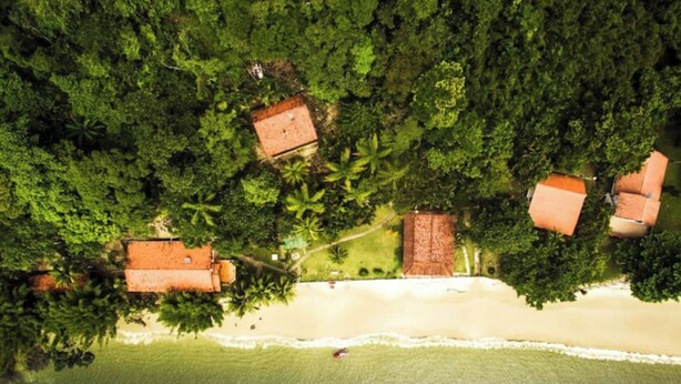 An aerial view of a coastal area with several buildings surrounded by dense greenery and a beach. - Accès Direct à la Plage - Suite Île (Itacuruçá)