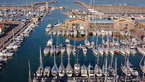 Un port esportiu amb nombroses embarcacions amarrades, un edifici central i una vista despejada del mar.