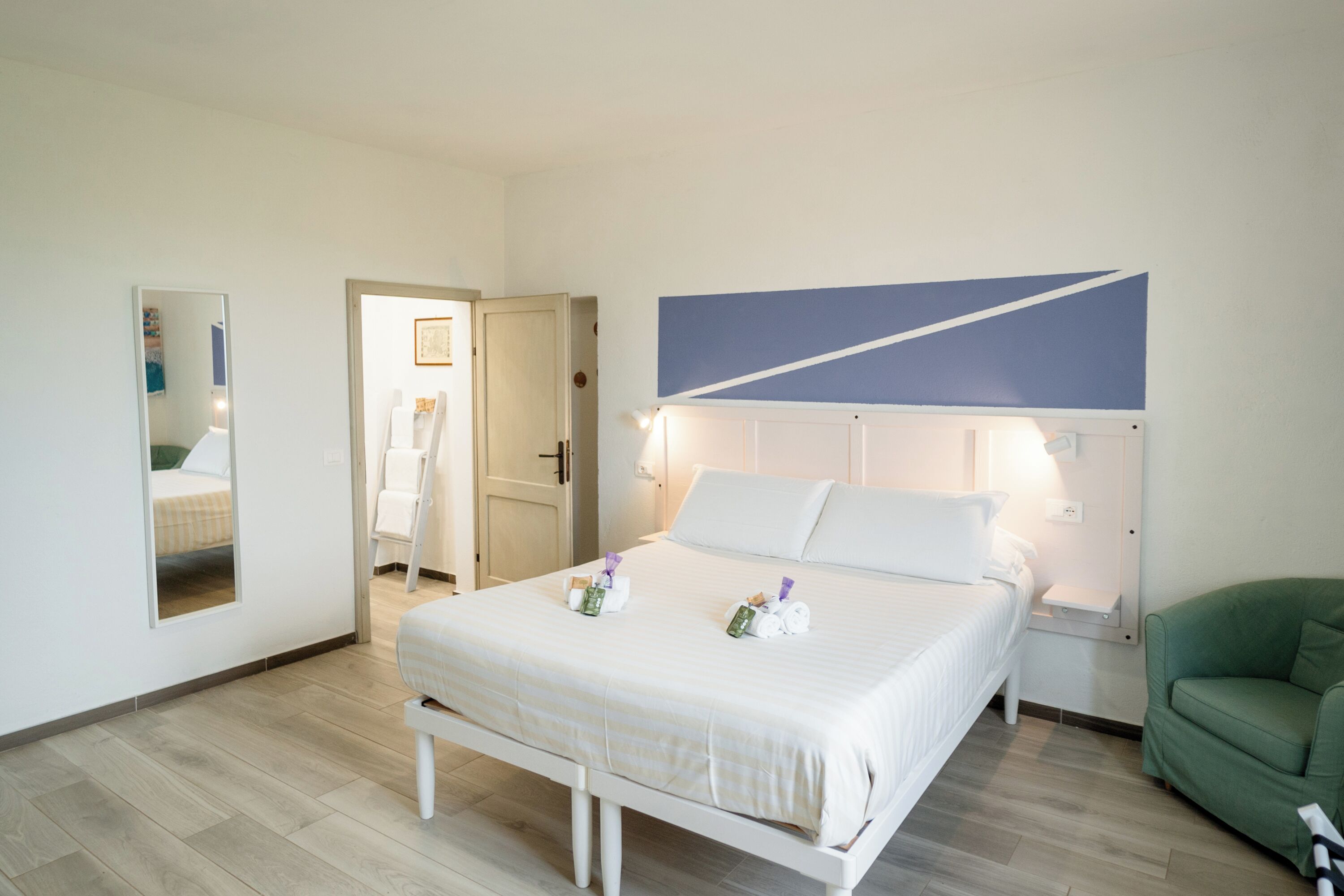 A hotel room with a bed, a green armchair, a nightstand, and a mirror.