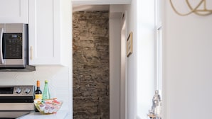A kitchen with white cabinets, a microwave, and a stone wall in the background.