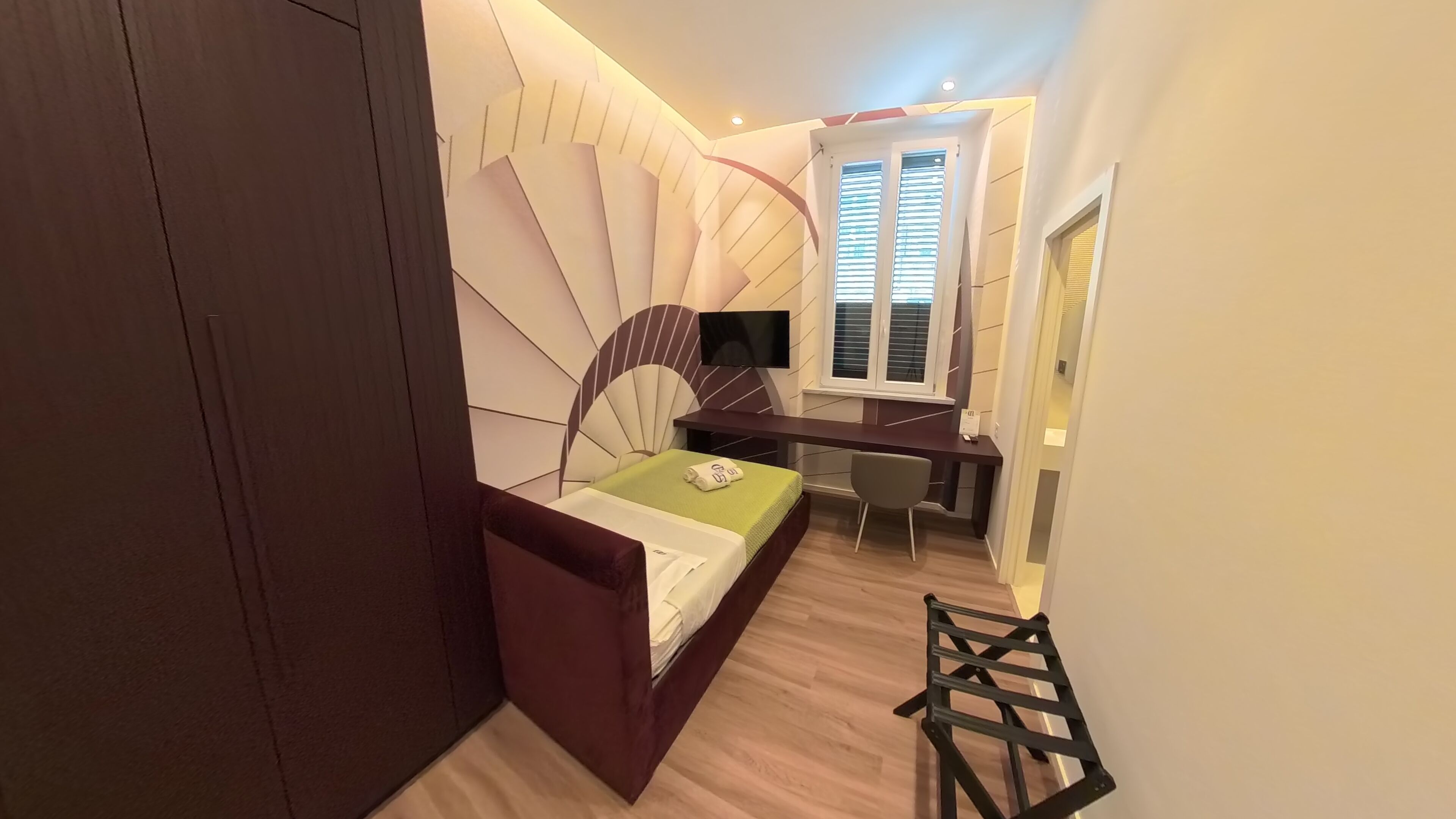 A bedroom with a bed, a desk, a chair, and a TV.