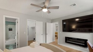 Une chambre à coucher avec un lit, un ventilateur de plafond, une télévision et une cheminée.
