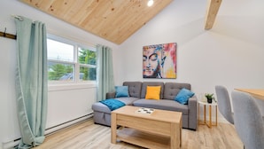 Een moderne woonkamer met een houten plafond, een grijze bank met kleurrijke kussens, een houten salontafel en een schilderij aan de muur.