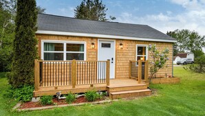 Een gelijkvloers houten huis met een veranda, een garage en een kleine tuin.