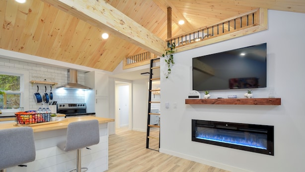 Een moderne keuken met houten balken in het plafond, een televisie boven een open haard en een bar met krukken.