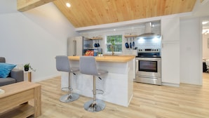Een moderne keuken met een houten plafond, een witte betegelde spatwand, roestvrijstalen apparatuur en een bar met twee krukken.