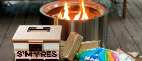 Un kit de S'mores, una barra de chocolate Hershey's y un malvaviscoo Jet-Puffed sobre una mesa de madera con un brasero al fondo.