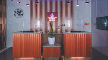 A reception desk with a neon sign, a clock, and a potted plant.