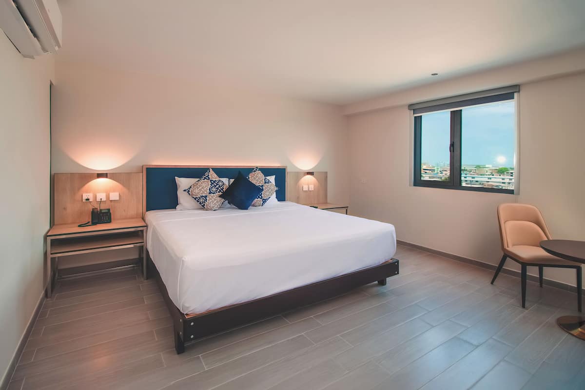 Une chambre d’hôtel avec un grand lit, des lampes de chevet, une chaise et une fenêtre donnant sur la ville.