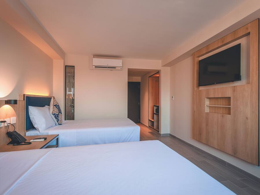 Une chambre d’hôtel avec deux lits, un téléviseur fixé au mur, une table de chevet avec un téléphone et un appareil de climatisation.