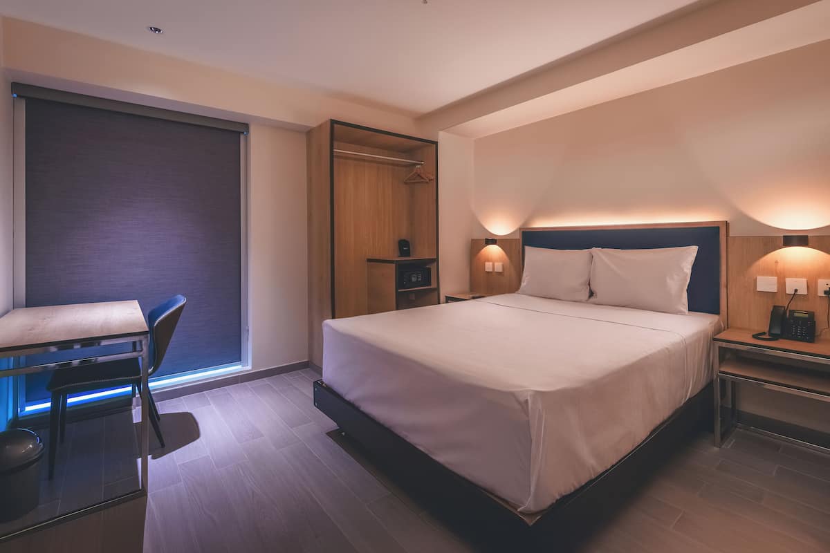 Une chambre d’hôtel moderne, dotée d’un grand lit, de tables de chevet, d’un bureau et d’une chaise.