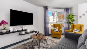 Ein modernes Wohnzimmer mit Flachbildfernseher, Couchtisch, Sofa und einem gelben Sessel.