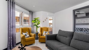 Ein modernes Wohnzimmer mit einem grauen Sofa, zwei senffarbenen Sesseln, einem Holztisch und einer Topfpflanze.
