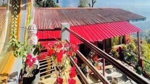 Un espacio exterior cubierto con una estructura de techo rojo, plantas en macetas y vistas a un paisaje lejano.