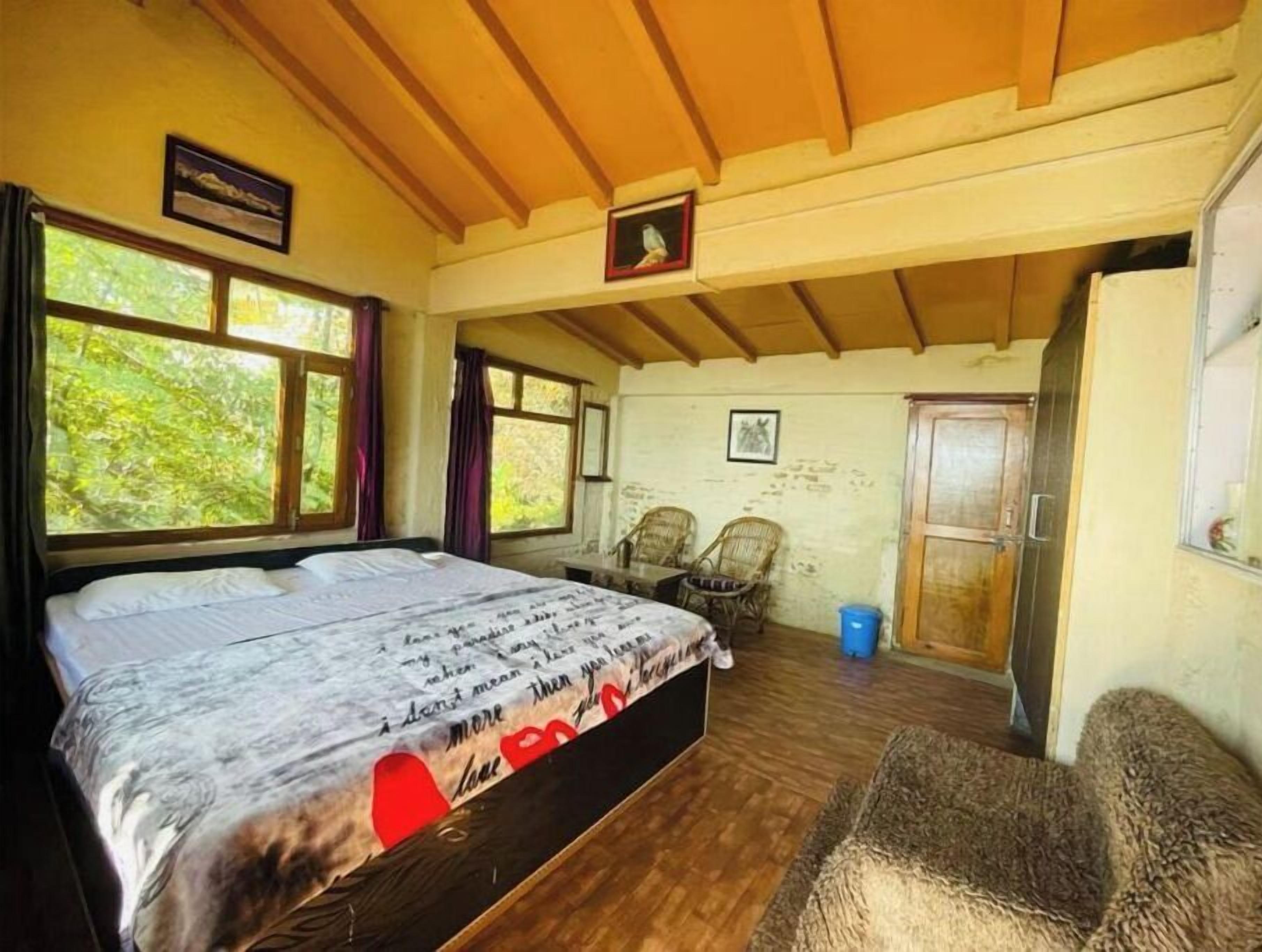 A bedroom with a large bed, two chairs, a wooden door, and a window with curtains.