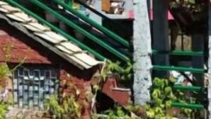 Ein Gebäude mit rotem Dach, einer Treppe, die zu einer Veranda führt, und einer kleinen Struktur mit blauem Markisen
